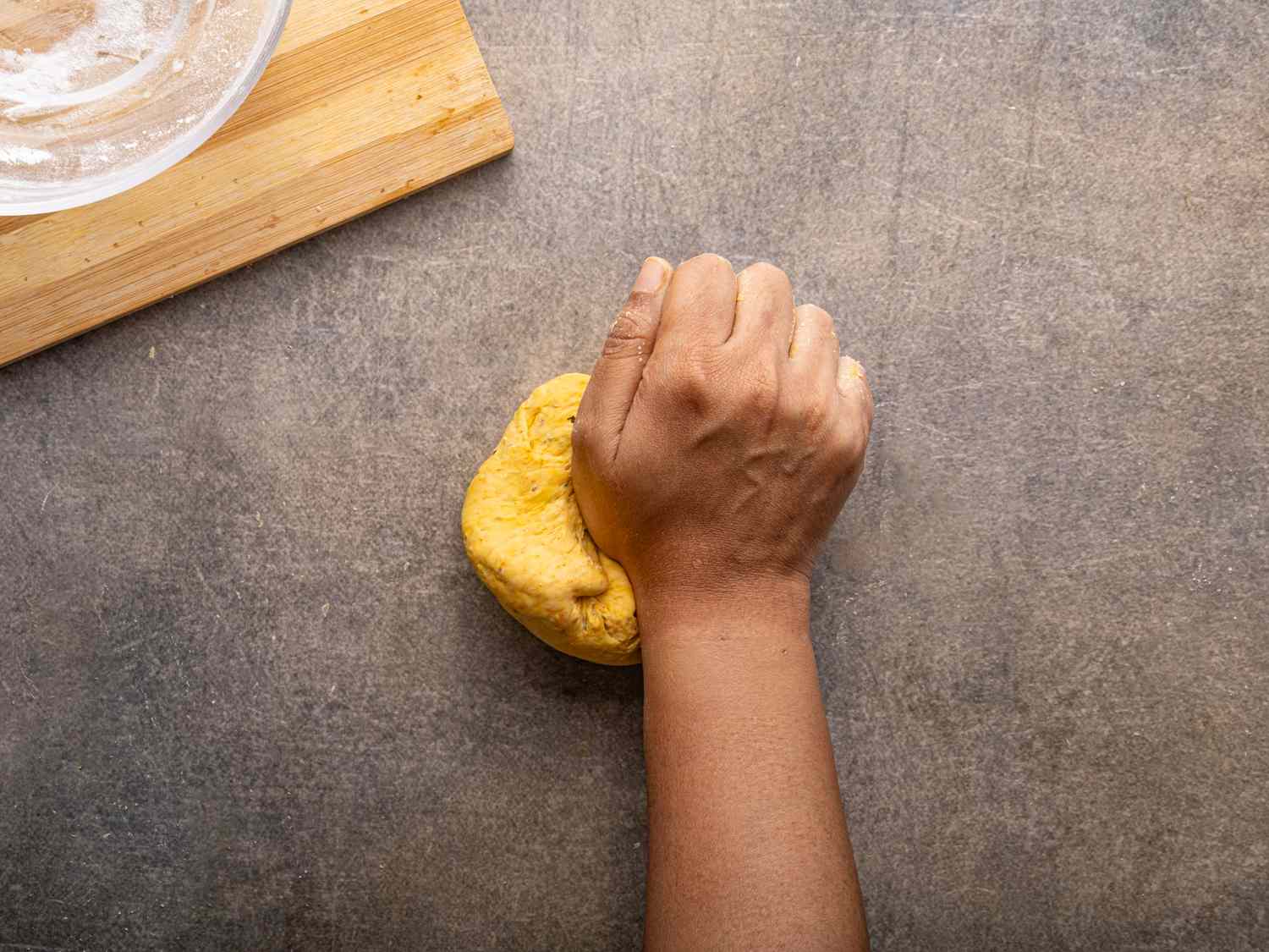 A hand kneading dough on a countertop with a cutting board nearby