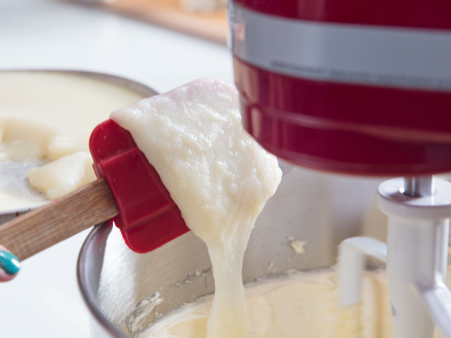 A spatula holding the milk paste and butter mixture being whipped in a stand mixer. 