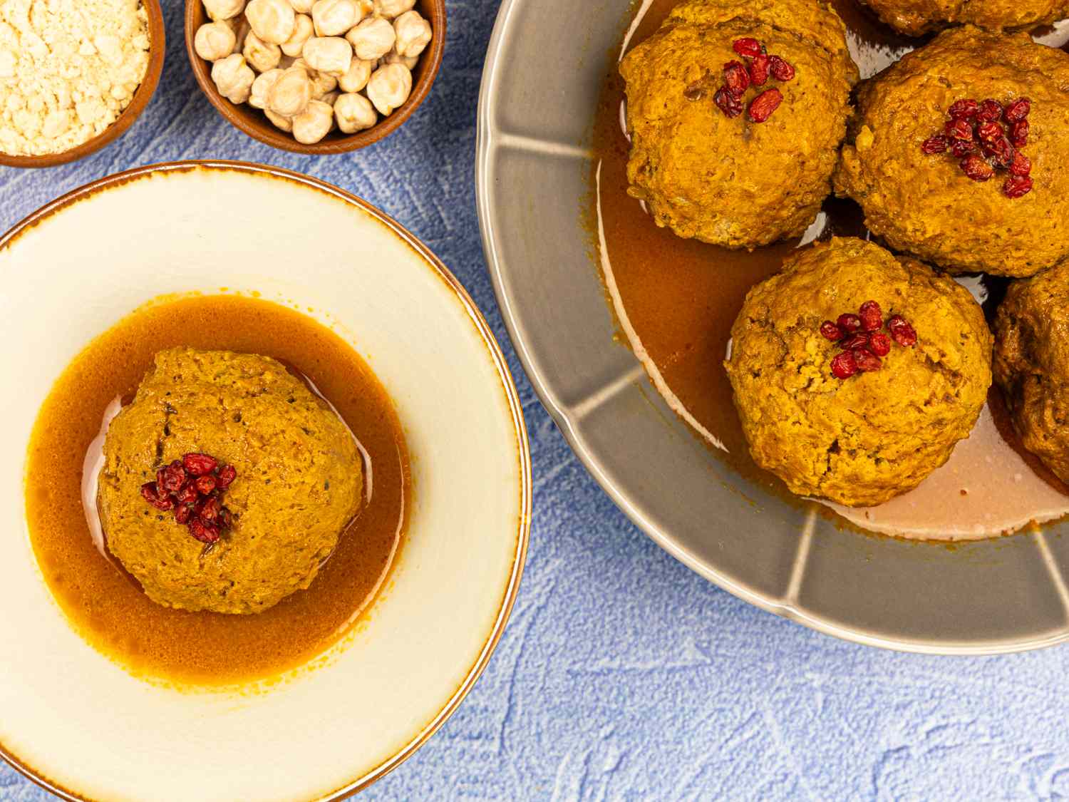 A plate and bowl of food featuring round dishes garnished with barberries with hazelnuts and powder in small bowls nearby