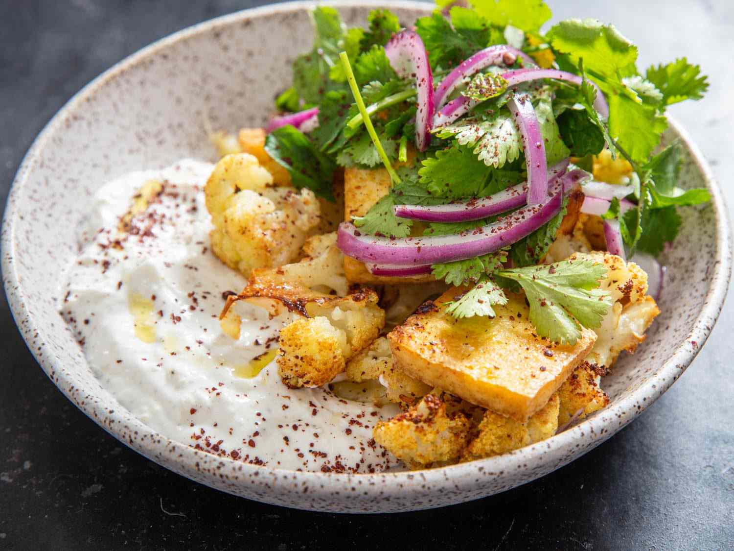 Roasted cauliflower and tofu with ginger-yogurt in a shallow bowl