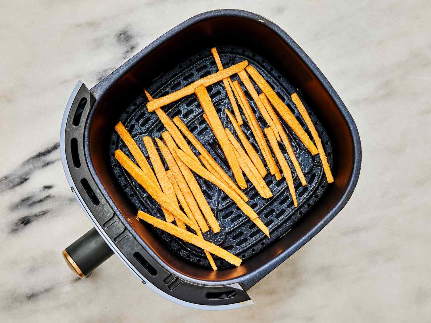 Air fryer basket with fries, spratyed with cooking spray