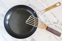 A ceramic frying pan with a metal fish spatula placed on top on a marble surface