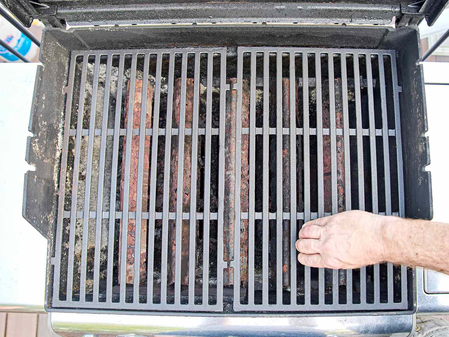 A hand hovering above the grill grates of a lit barbecue grill