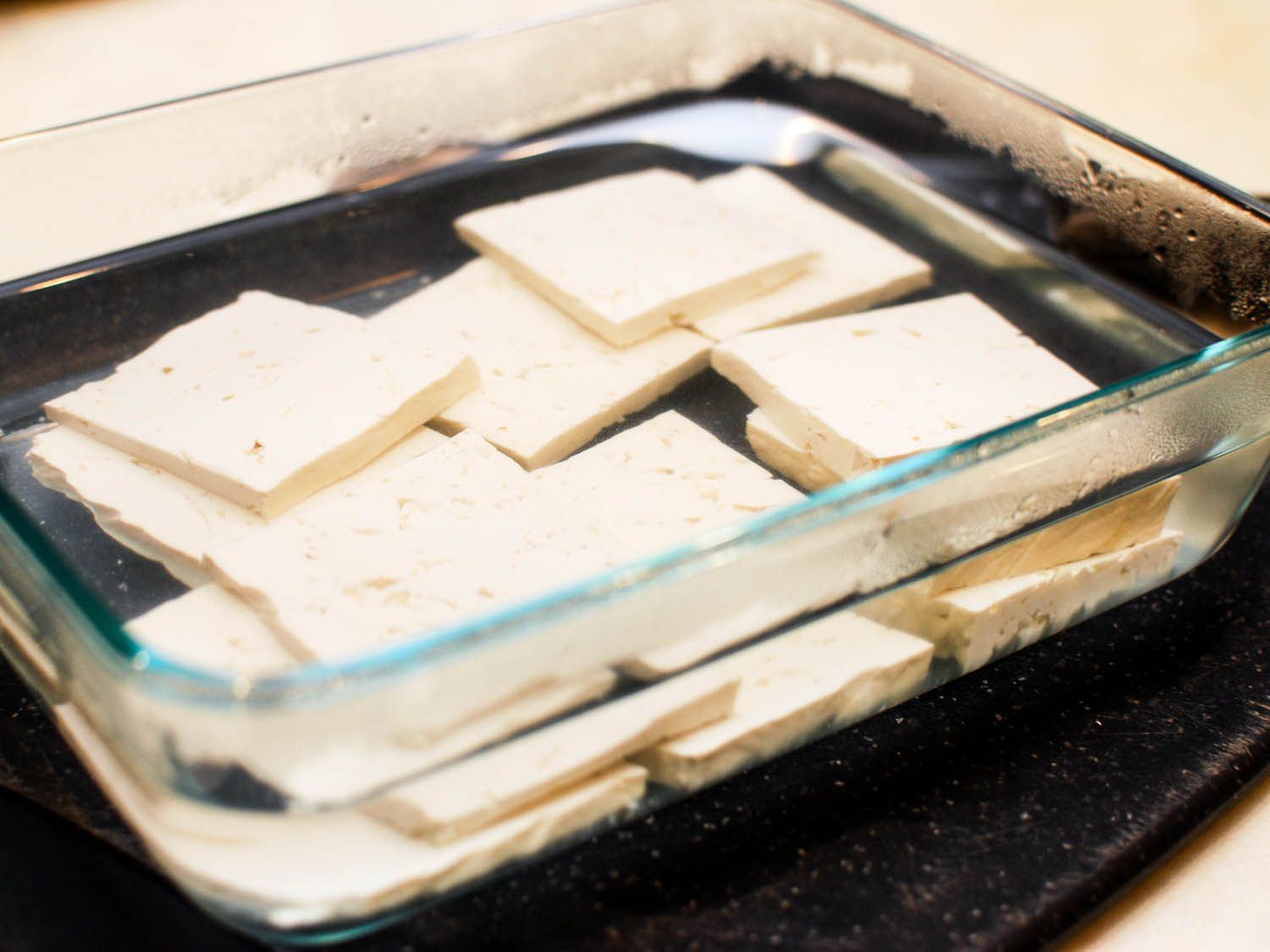 slices of tofu soaking in glass dish full of hot water