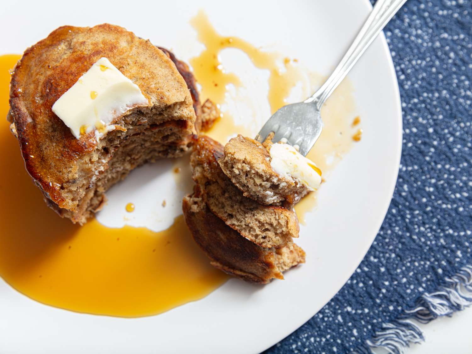 Overhead angle of stack of pancakes with part cut out on a fork on a blue fabric surface