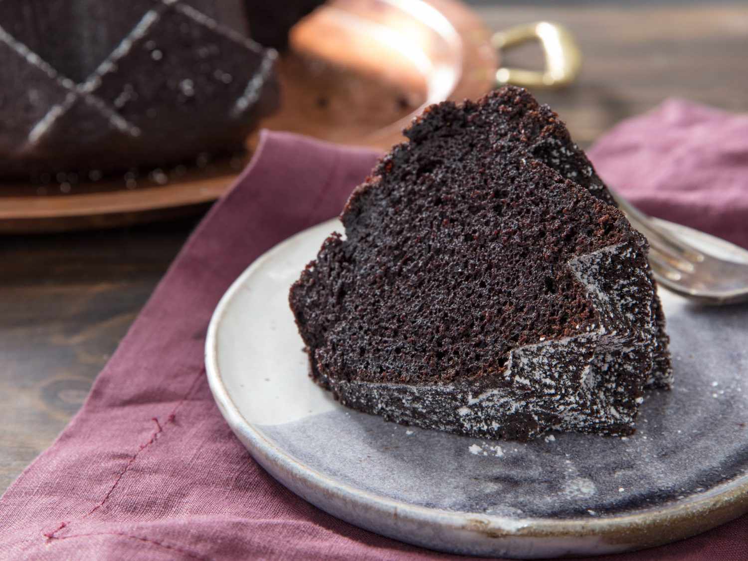A slice of chocolate bundt cake on a ceramic plate.