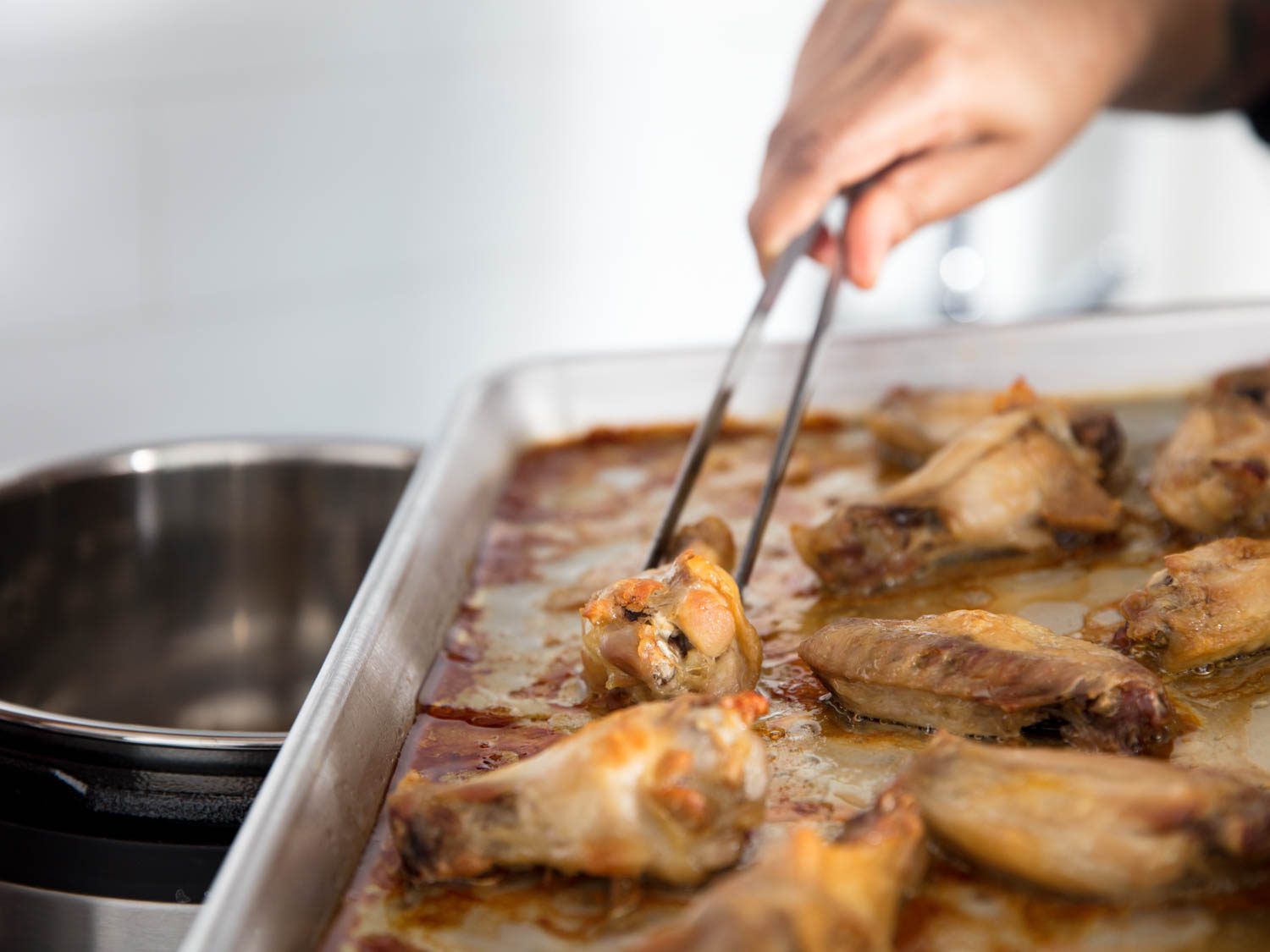 The roasted chicken wings are transferred to a pressure cooker with a large pair of culinary tweezers.