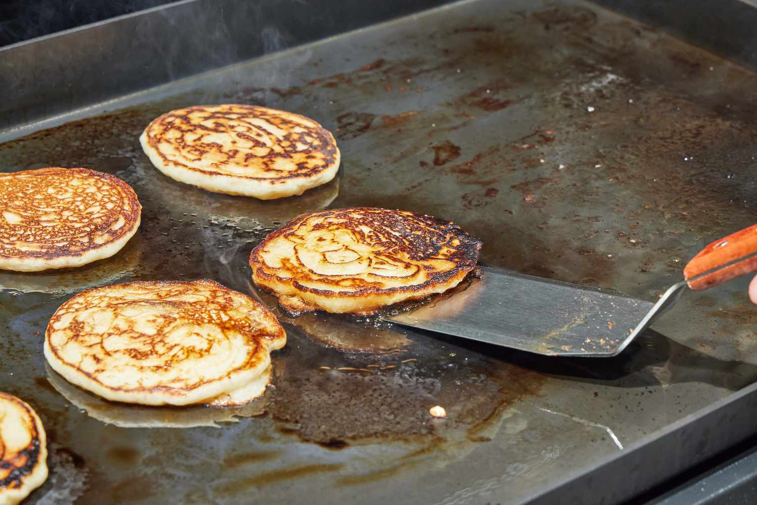 A person flips pancakes cooked on the Weber Slate 30 Inch Griddle