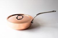 Copper saucepan with a lid and a long stainless steel handle placed on a white background