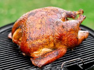 A golden Cajun-style turkey resting on the surface of a charcoal grill.