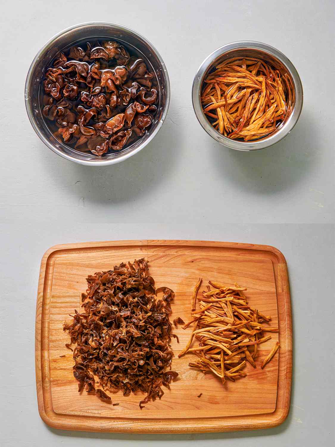 A two-image collage. The top image shows two metal mixing bowls side by side, one of which holds wood ear mushrooms soaking in water, the other of which holds dried day lily bulbs soaking in water. The bottom image shows a wooden cutting board holding the soaked and now slivered wood ear mushrooms and day lily bulbs.
