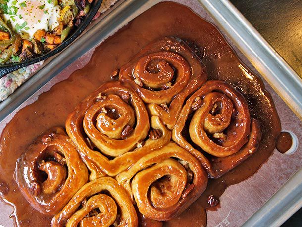 A tray of Bravetart sticky pecan buns in a pool of extra caramel.