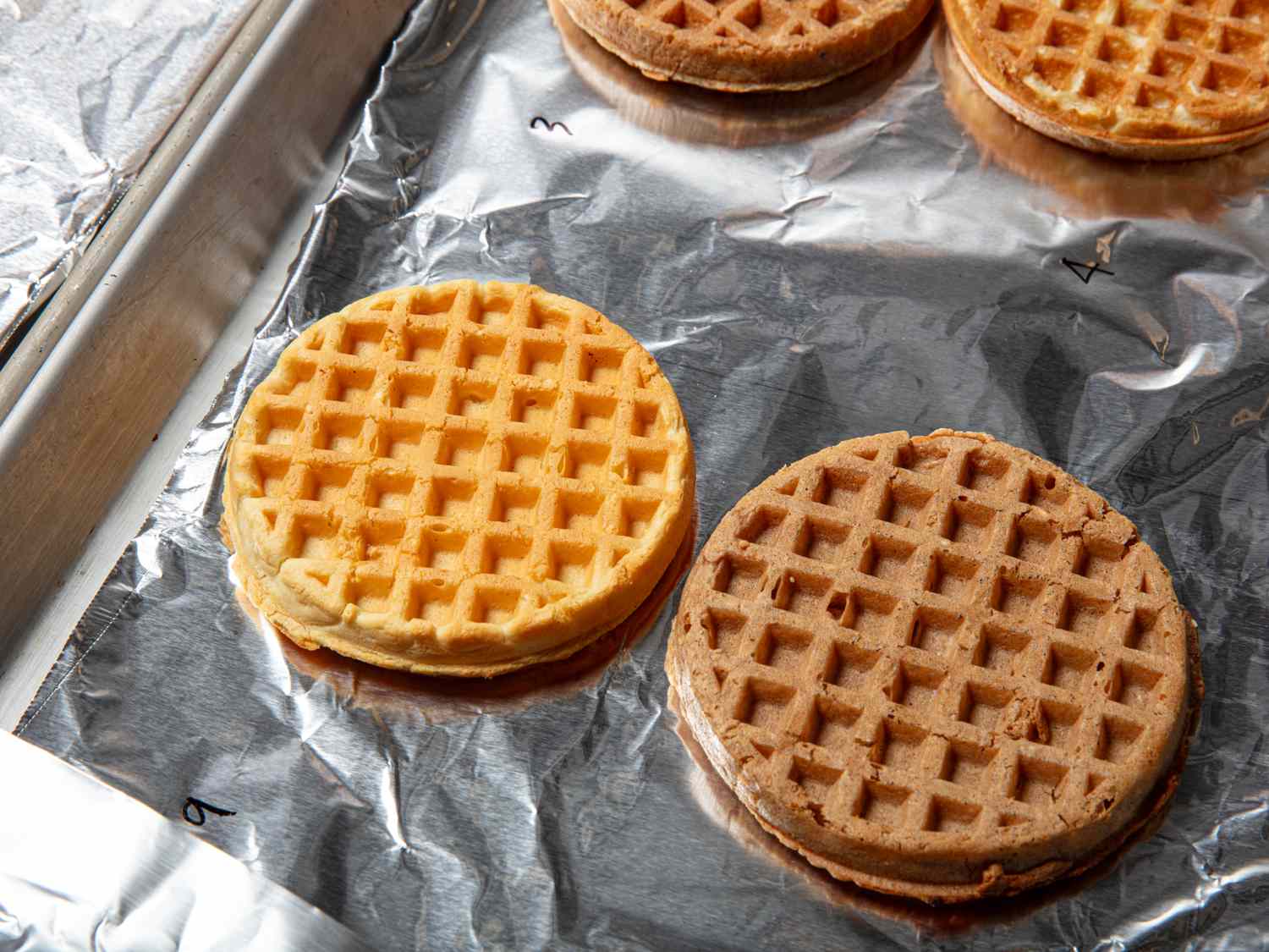Two waffles placed on a baking sheet lined with foil with more waffles in the background