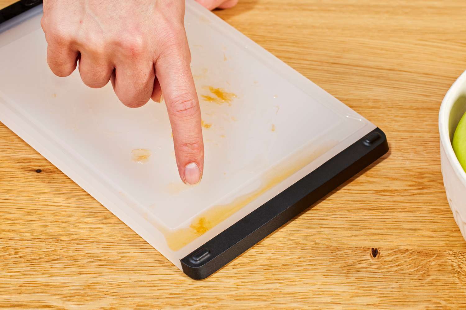 A hand pointing at residue on a chopping board next to fruit in a bowl