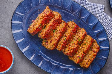Slices of meatloaf arranged on a serving plate accompanied by a bowl of sauce beside it