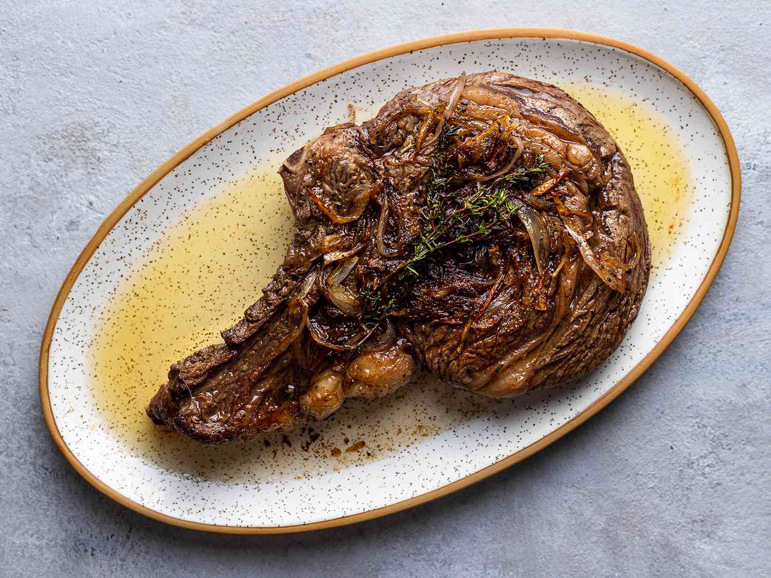 The steak, fully cooked and basted with butter, sitting on a platter with cooking juices.