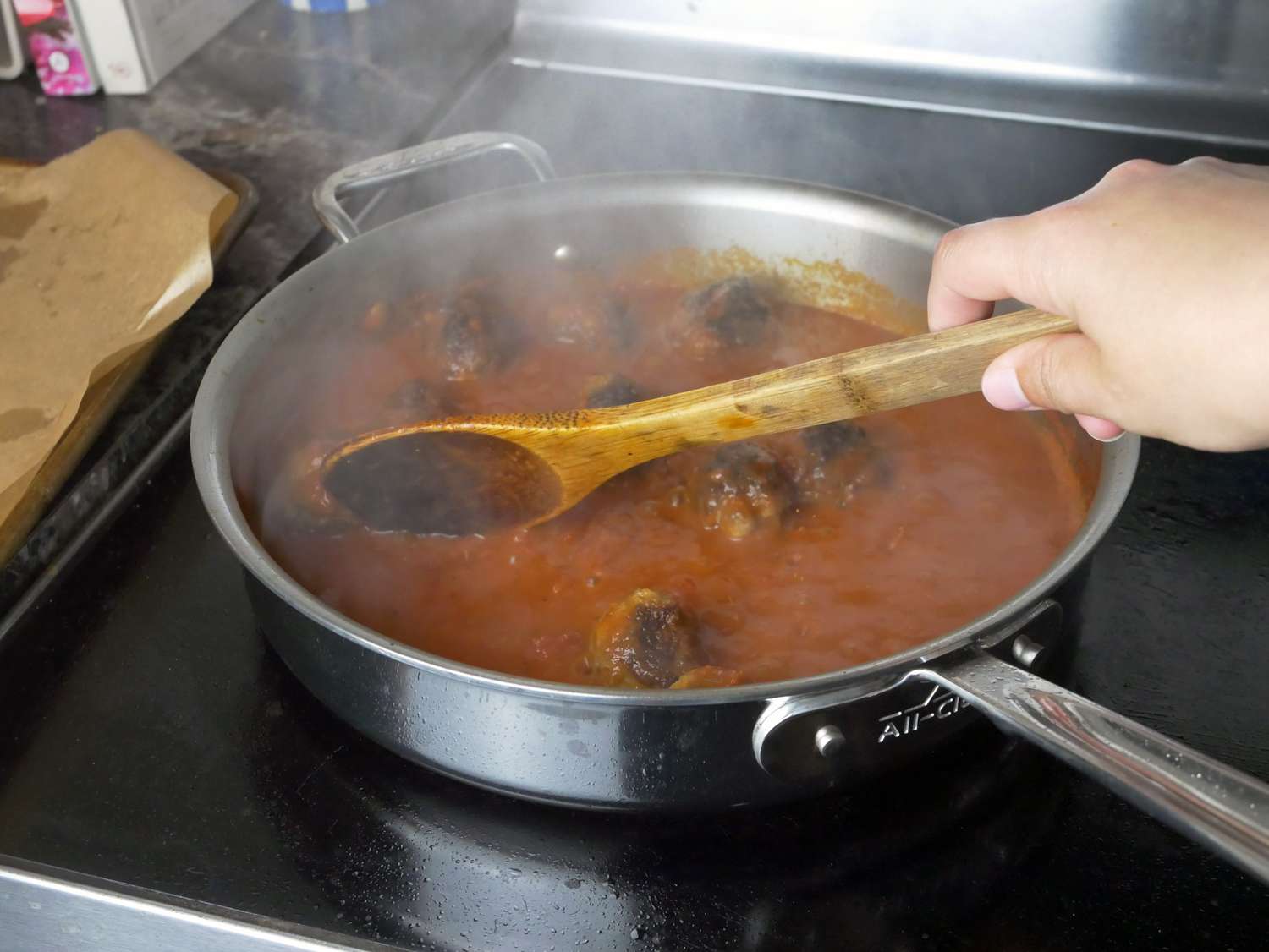 a person stirring tomato sauce with meatballs in a saute pan