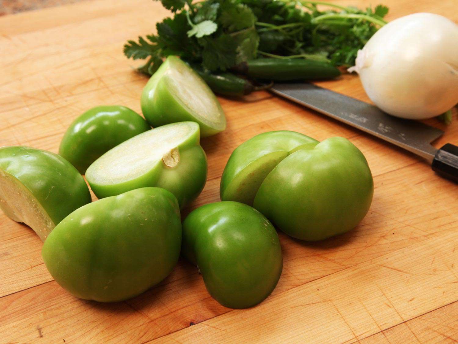 Tomatillos split in halves on a cutting board. 