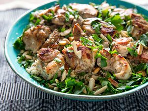 Broiled tandoori chicken, served in a blue bowl over couscous and garnished with slicered almonds and herbs.