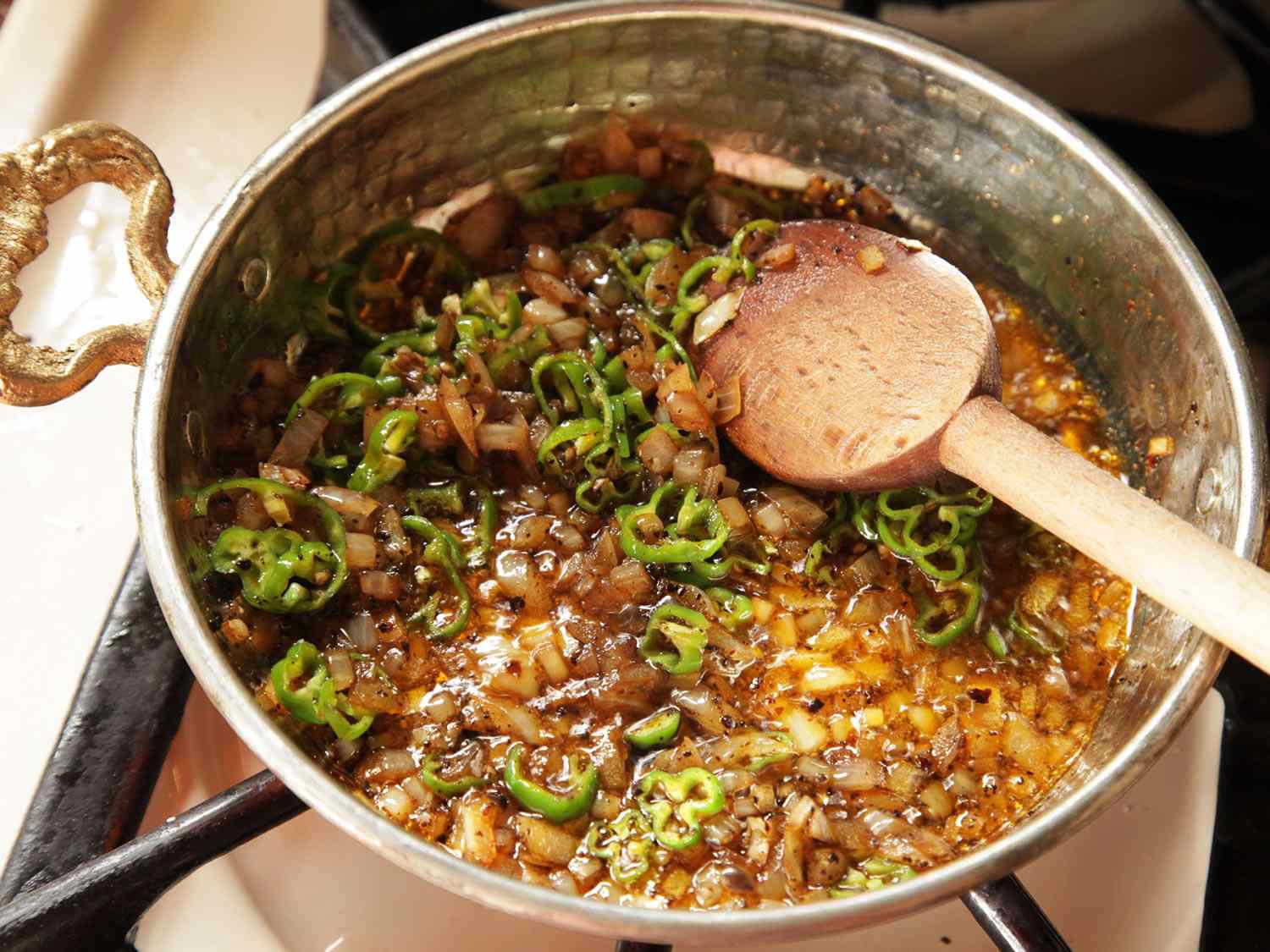 Slow-cooking shishito peppers with onions and tomatoes for menemen