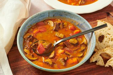 Kansas City Steak soup in bowl on wooden board with spoonful of soup, bread, and another bowl in thebackground