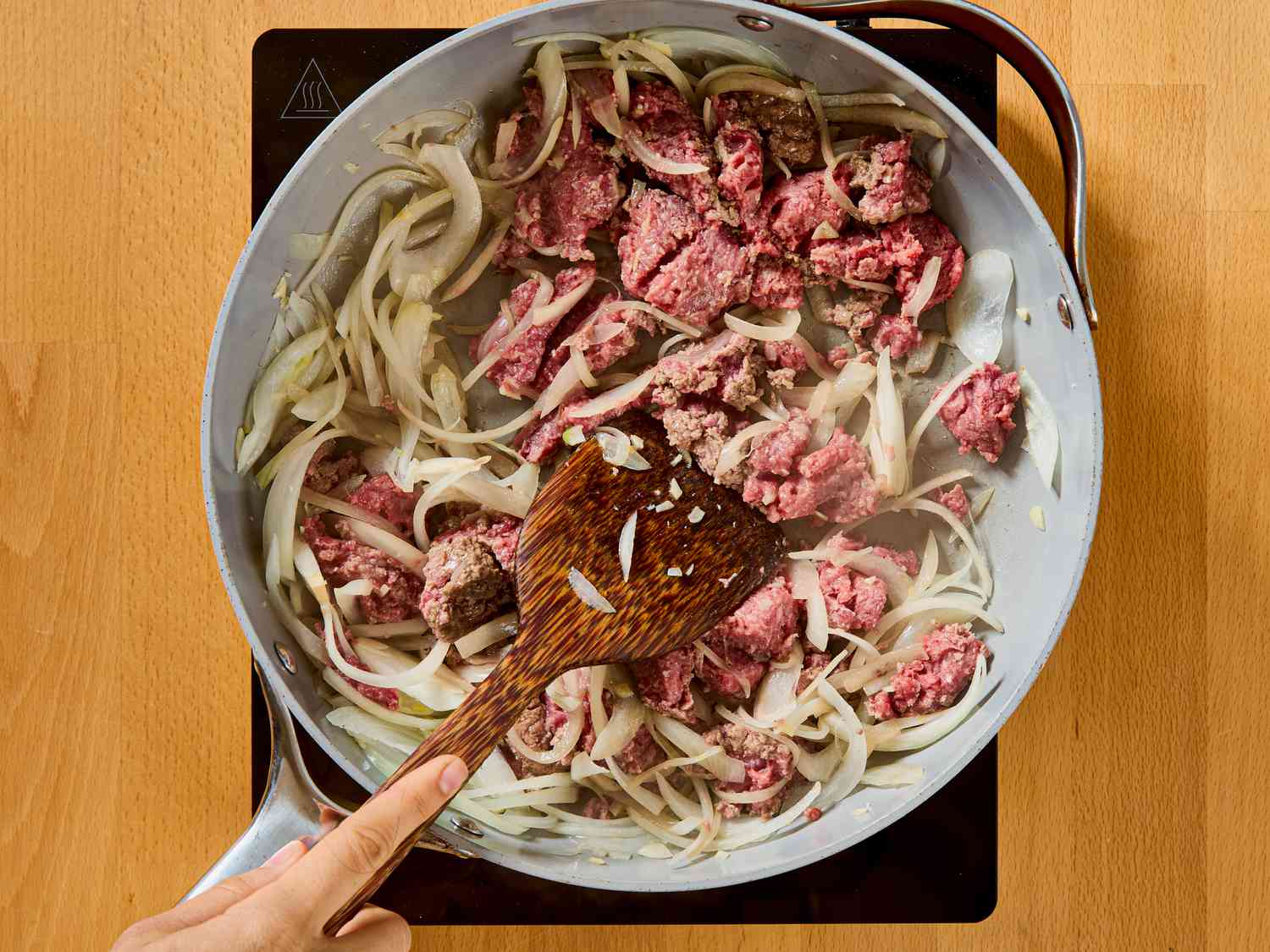 Cooking ground meat and onions in a skillet using a wooden spatula