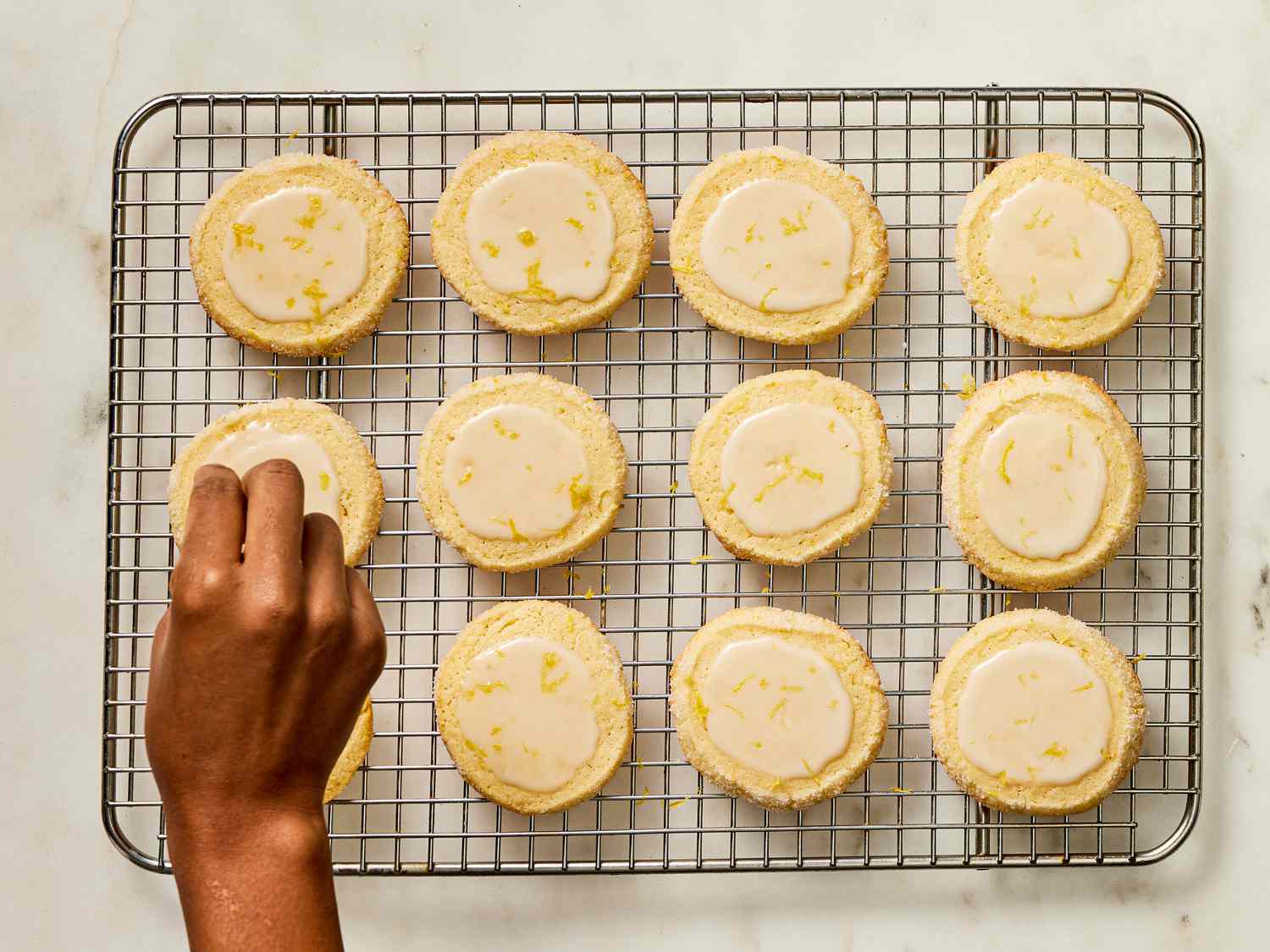 hand garnishing glazed cookies with lemon zest, while they are on cooling rack 