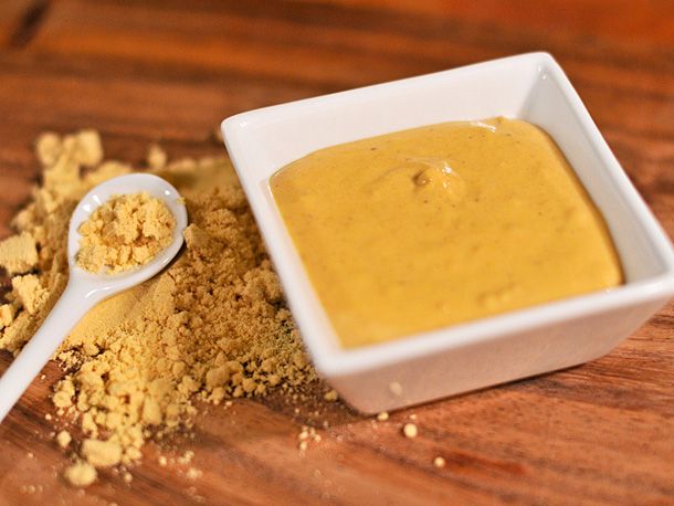 A bowl of hot mustard next to some mustard powder. 
