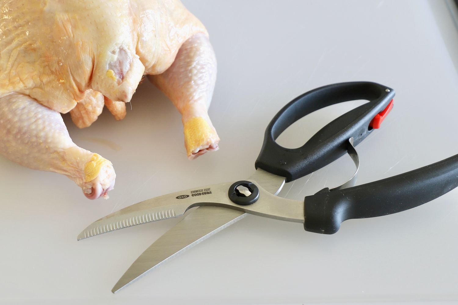Poultry shears on a cutting board beside a whole chicken.