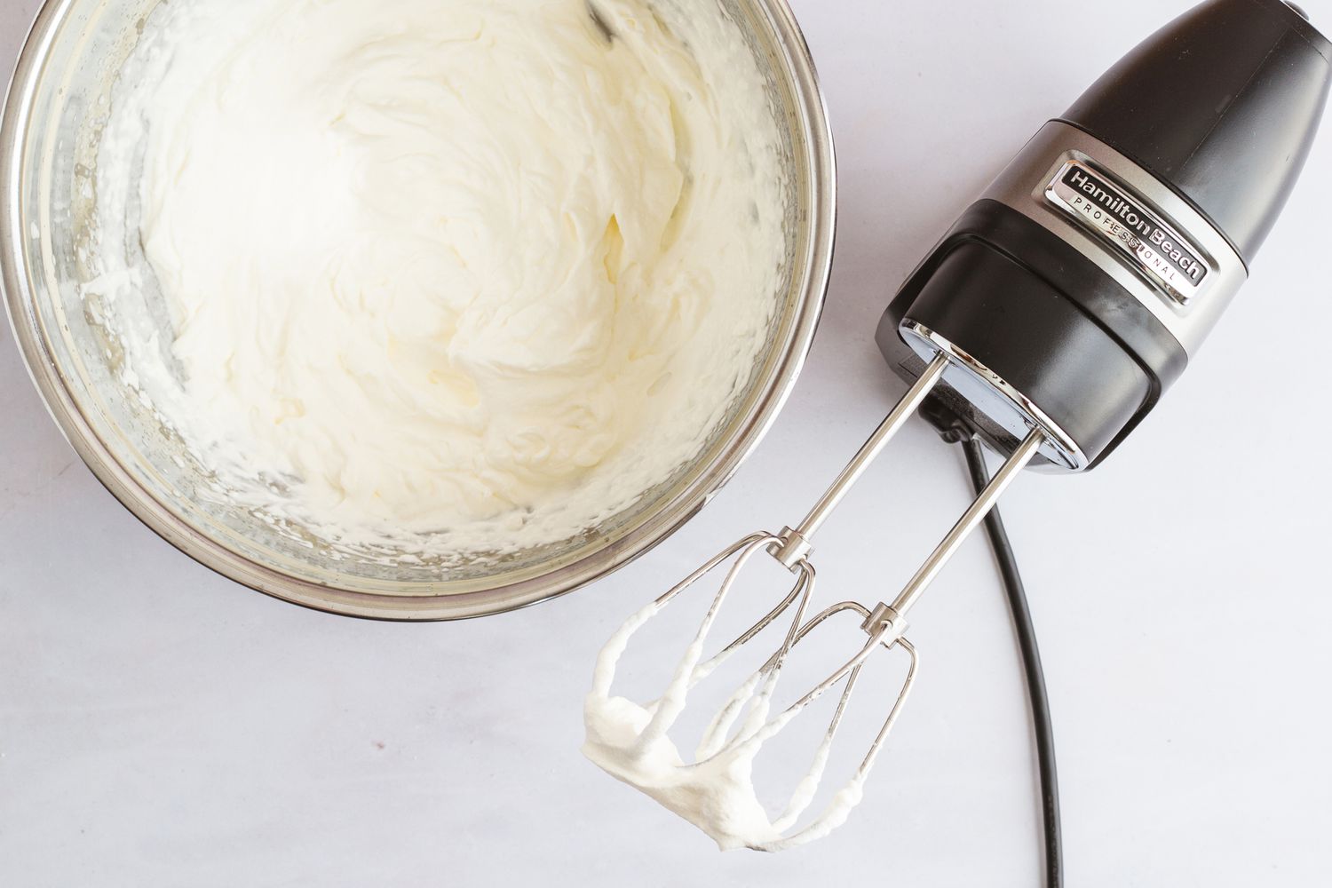 A hand mixer beside a bowl of whipped cream.