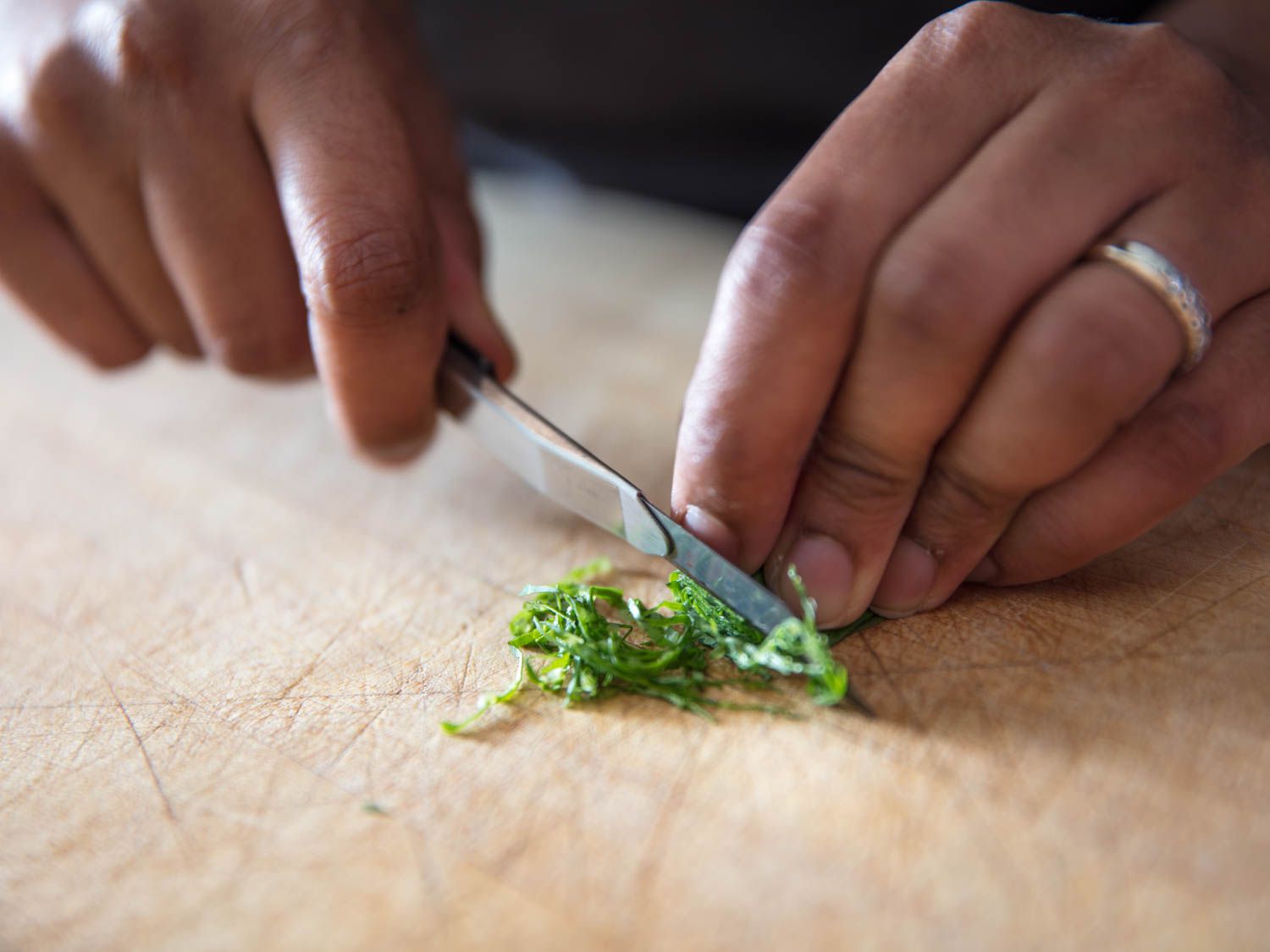 Using a utility knife to finely slice herbs on a wooden surface