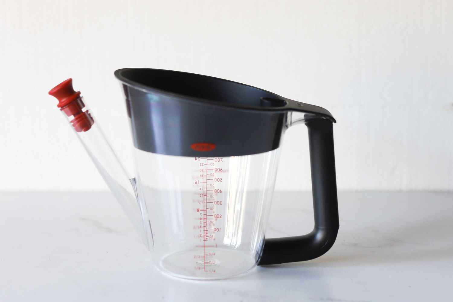 A measuring cup with a black handle and a spout equipped with a red plunger mechanism