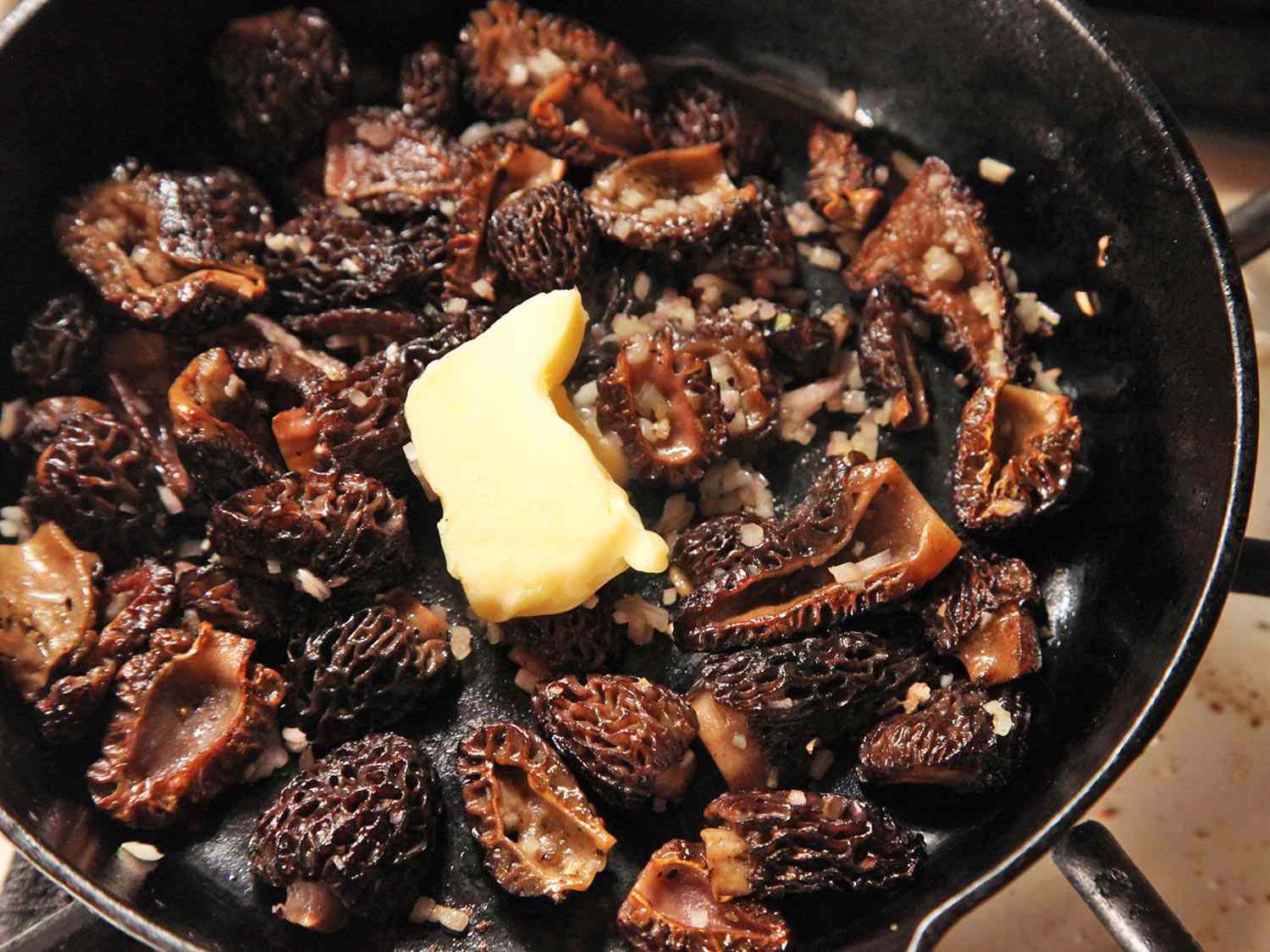 A pat of butter over sautéed morel mushrooms in a skillet.
