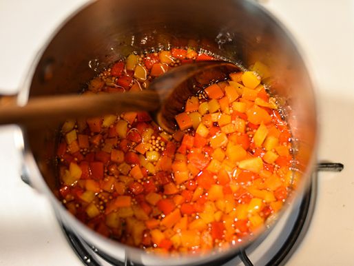 Stirring finished pepper relish in a pot with a wooden spoon.