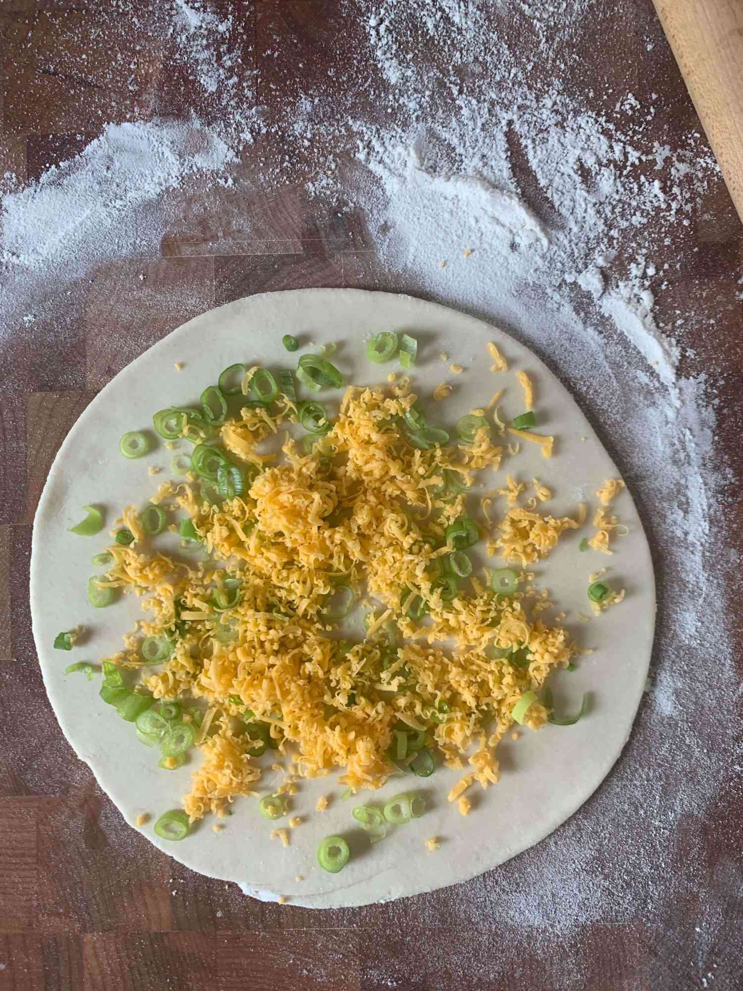 scallion pancake dough with scallions and cheese sprinkled over it