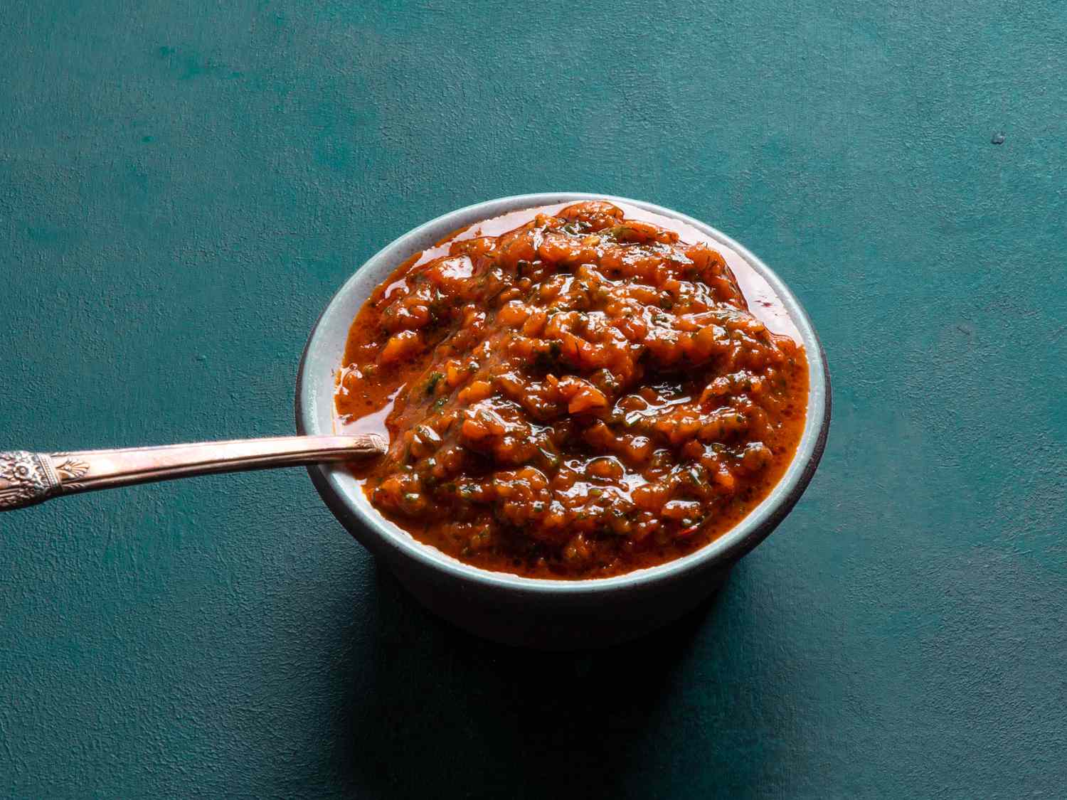 A small dish holds a deep red, rough red pepper puree, flecked with minced herbs.