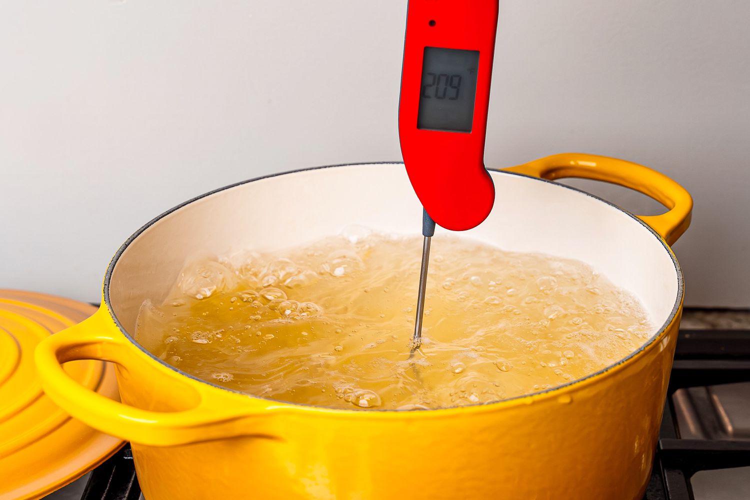 An instant-read thermometer testing the temperature of water in a yellow enameled cast iron Dutch oven.