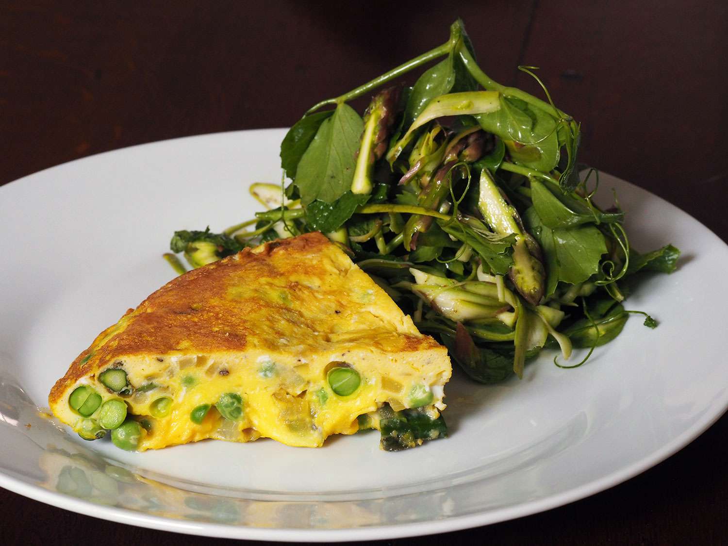 A slice of finished frittata is plated with the salad.