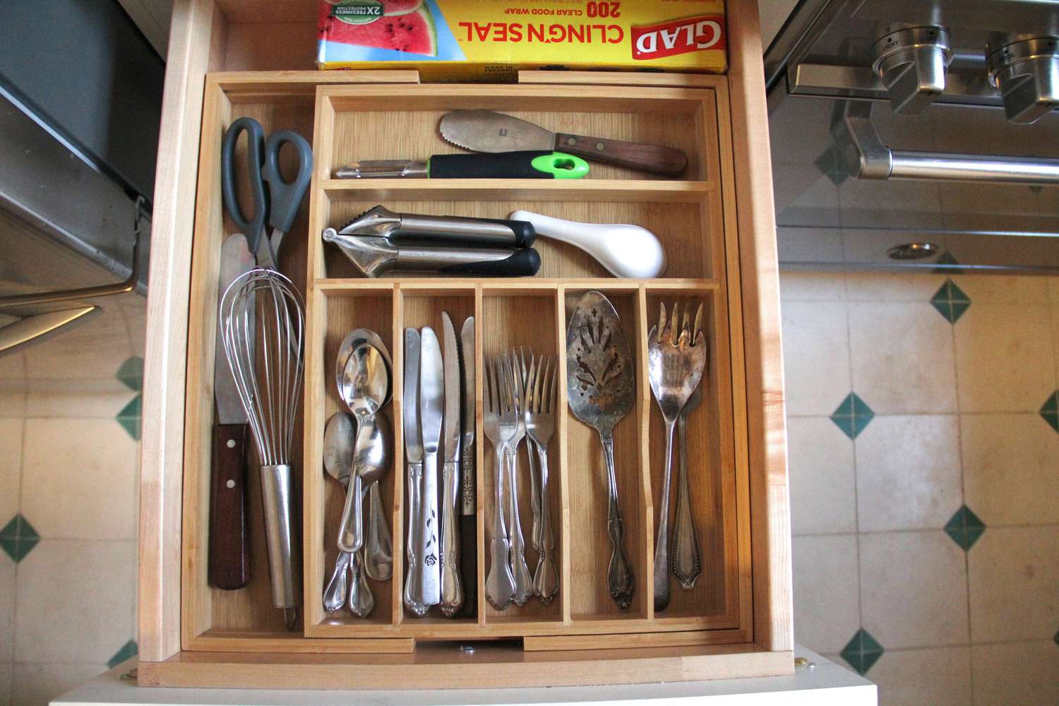 A kitchen drawer organizer filled with silverware and kitchen utensils in a drawer by the stove.