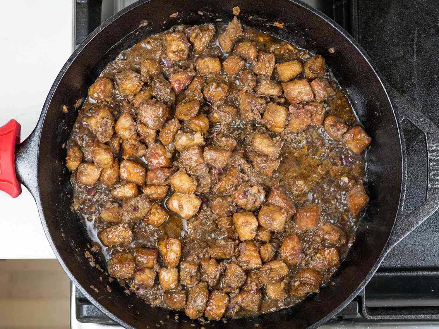 The fried pork pieces and sauce being cooked together in a cast iron pan.