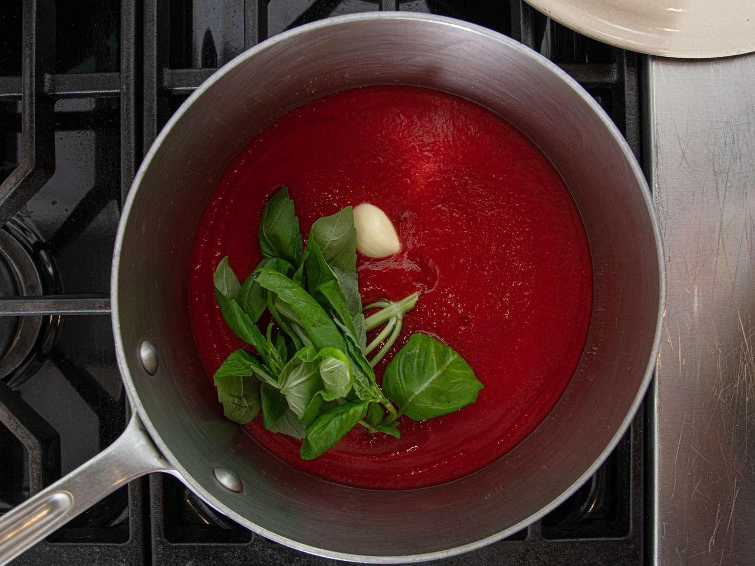 A saucepan with tomato sauce fresh basil and a garlic clove on a stovetop