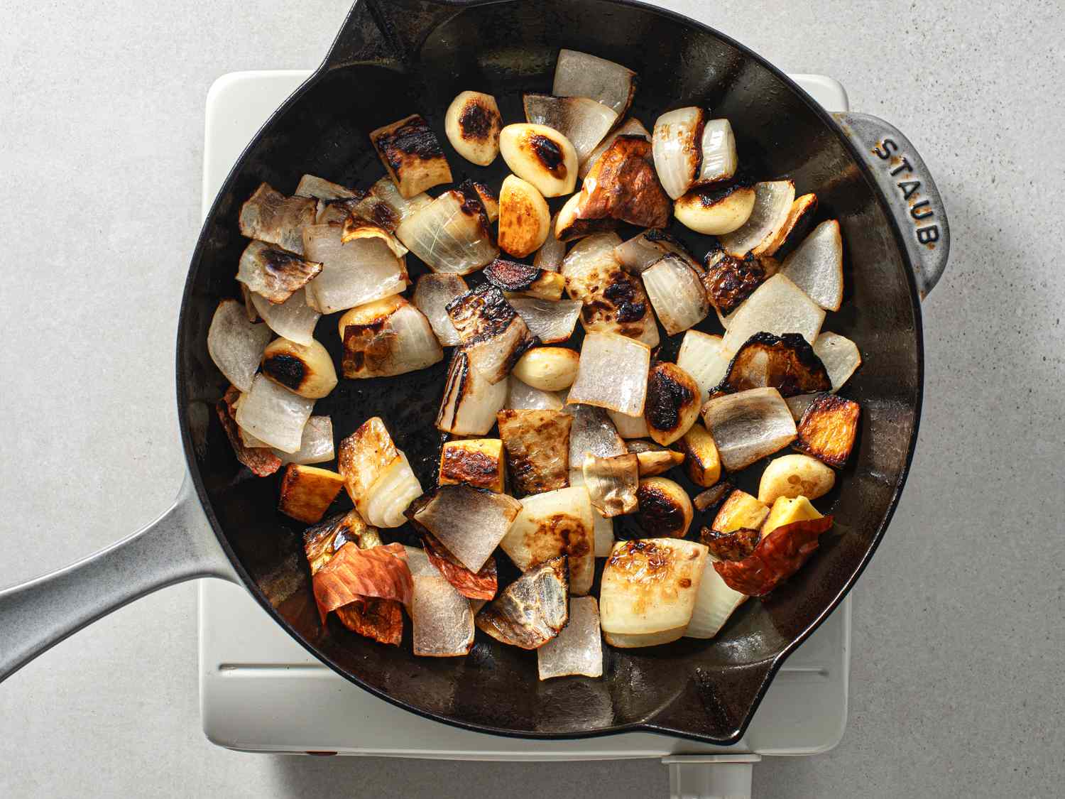 Roughly chopped onion, garlic cloves, and roughly chopped ginger deeply charred on most sides in a medium cast iron skillet.