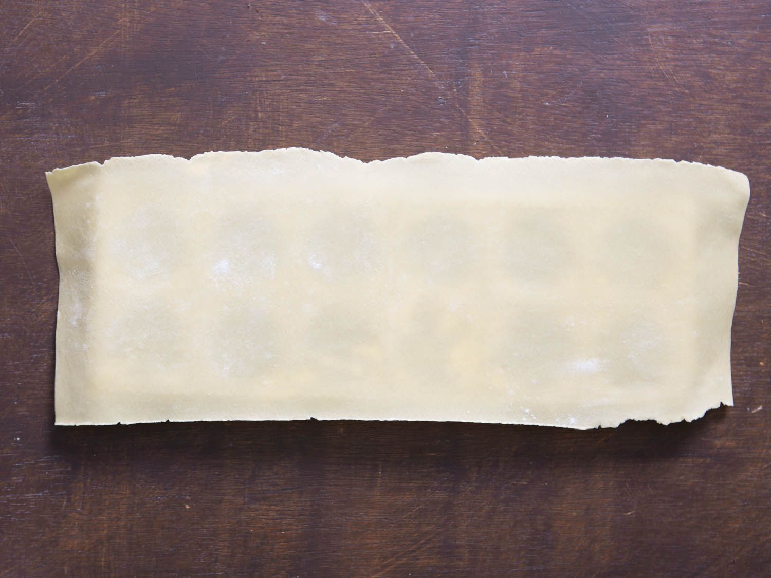 A thin sheet of fresh pasta cut to size is placed over a ravioli mold.