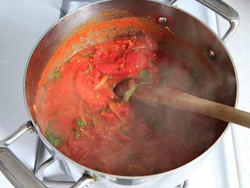 A simmering pot of masala sauce, adding cilantro and stirring with a wooden spoon.