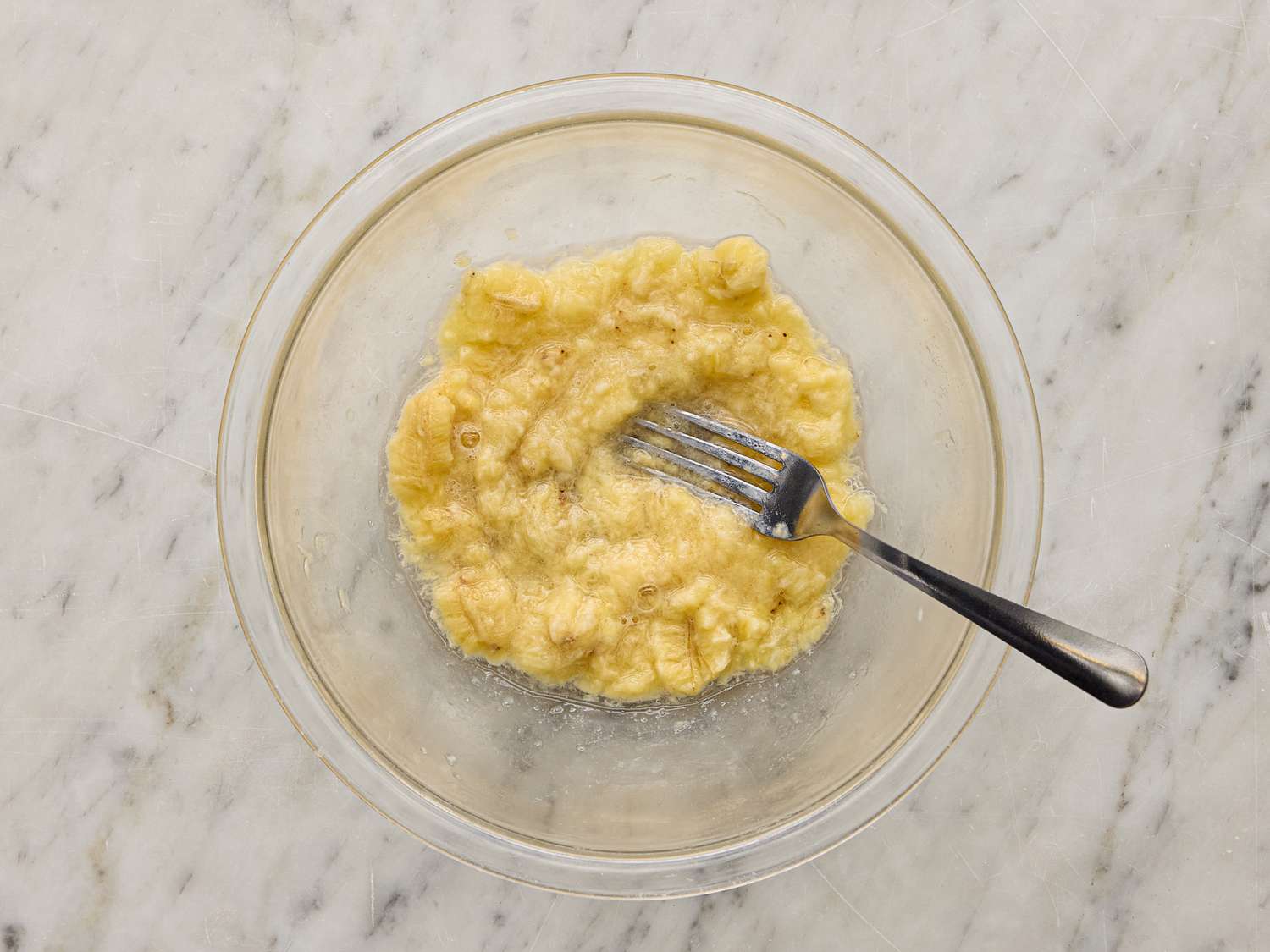 Mashed bananas in a glass bowl with a fork