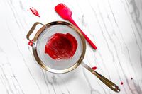 All-Clad Stainless-Steel Strainer, Set of 3 containing red puree placed on a marble surface with a red spatula next to it