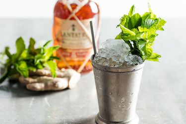 A dark and stormy julep cocktail, served in a silver julep cup, garnished with a large bouquet of mint sprigs.