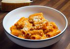 A white bowl of penne alla vodka sprinkled with cheese