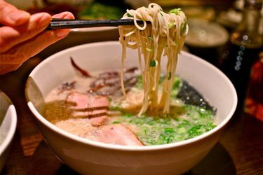 A bowl of ramen. Someone is using chopsticks to lift noodles above the bowl. 
