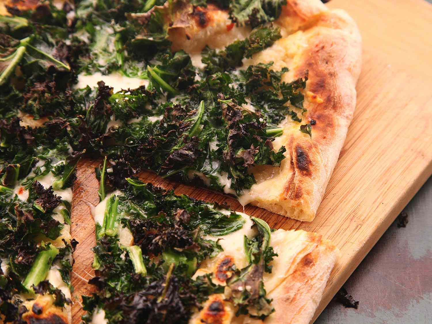 A finished kale pizza with garlic on a serving platter. 